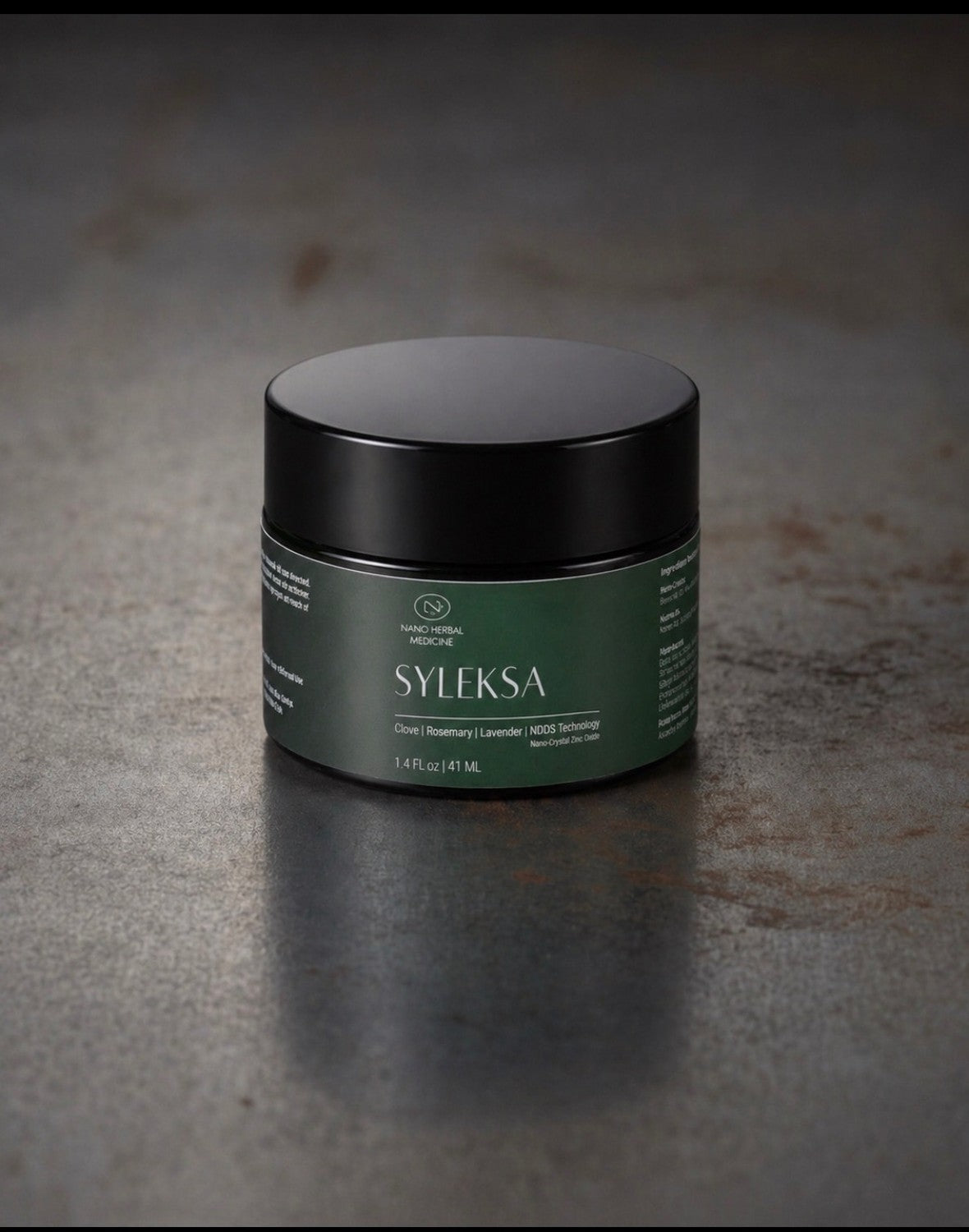 SYLEKSA Nano Herbal Cream jar — matte black lid and deep green label on a dark metal surface, studio lighting